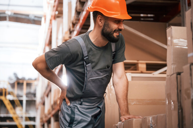 Warehouse employee resting against a box, holding back in pain