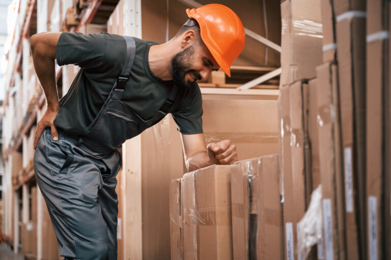 Warehouse worker clutching back while leaning on box